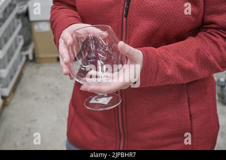 Das kaukasische Mädchen kauft ein großes, transparentes Glas für Wein und Brandy in einem Geschäft Stockfoto