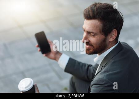 Lächelnder Büroangestellter in Anzug, der während der Pause auf der Treppe mit Kaffee sitzt und telefonieren muss Stockfoto