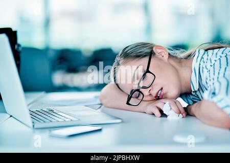 Es war ein langer Tag. Eine müde aussehende junge Geschäftsfrau schlief tagsüber auf ihrem Schreibtisch im Büro bei der Arbeit. Stockfoto