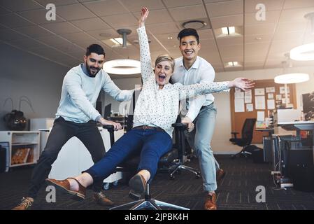 Die sagten, dass das Büro nicht lustig sein kann. Geschäftsleute, die Spaß haben, indem sie ihre Kollegin mit auf ihren Stuhl nehmen. Stockfoto