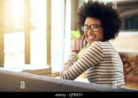 Nehmen Sie es heute schön und einfach. Porträt einer fröhlichen jungen Frau, die tagsüber bequem auf einer Couch zu Hause sitzt. Stockfoto