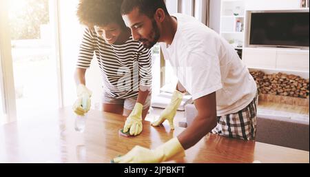 Honig vermisst Sie einen Platz. Ein fröhliches junges Paar Reinigung der Oberfläche eines Tisches mit Reinigungsgeräten zusammen zu Hause. Stockfoto