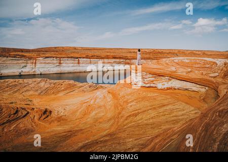 Erkunden Sie Das Glen Canyon National Recreation Area. Silhouette einer Frau, die auf einer Klippe steht, wellige rote Felsen und dramatischer wolkiger Himmel auf dem Hintergrund Stockfoto