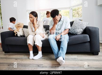Traurige, unglückliche und gestresste Eltern, die nach einem Streit auf einer Couch in der Nähe ihrer Kinder zu Hause sitzen. Frustriert, müde und verärgert sind Mama und Papa Stockfoto