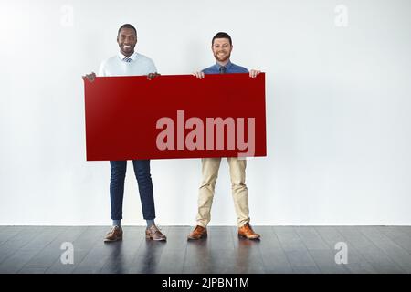Vielleicht empfehlen wir etwas Rot für deine Nachricht. Studioaufnahme von zwei Geschäftsleuten, die ein rotes, blank gehaltenes Plakat hochhielten. Stockfoto