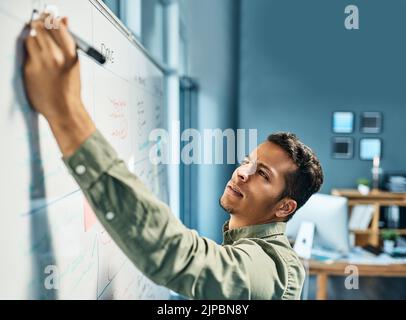 Wichtige Anpassungen in letzter Minute. Ein fokussierter junger Geschäftsmann, der tagsüber auf einem weißen Schriftzug im Büro steht. Stockfoto