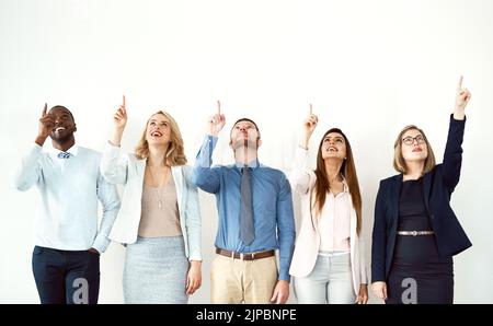 Schauen Sie in den Himmel. Eine Gruppe von Arbeitskollegen schaut nach oben und zeigt in Richtung Himmel, während sie vor einem weißen Hintergrund steht. Stockfoto