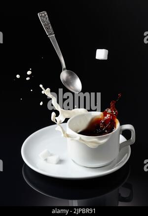 Tasse Kaffee auf einem schwarzen reflektierenden Hintergrund. Kaffee mit Milchspritzern. Stockfoto