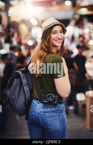 Es ist ein Hut tragen Art von Tag. Eine fröhliche junge Frau, die während des Tages auf einem geschäftigen Markt draußen herumläuft. Stockfoto