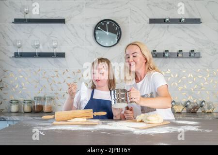 Mädchen mit Down-Syndrom und ihre charmante Mutter, backen Teigkuchen in der Küche Stockfoto