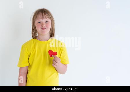 Süßes kleines Mädchen mit Down-Syndrom, spielt mit Papier Herz. Welt Down-Syndrom Tag Hintergrund. Down-Syndrom-Bewusstsein-Konzept. Stockfoto