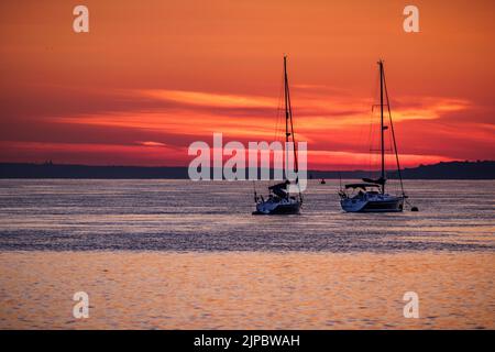Zwei Segelboote festgemacht auf dem Meer während eines lebhaften orangefarbenen Sonnenaufgangs Stockfoto