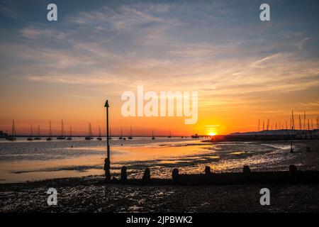 Wunderschöner Sonnenaufgang über dem Solent, mit den Booten, die vor der Küste von Yarmouth auf der Isle of Wight festgemacht wurden. Stockfoto