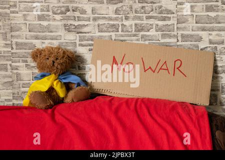 Stop war je geschrieben auf Schild die steht zu Hause in der Ukraine in der Nähe eines Teddybären mit Flagge der Ukraine. Frieden in der Ukraine. Protest. Russland ist der Aggressor 2022 Stockfoto