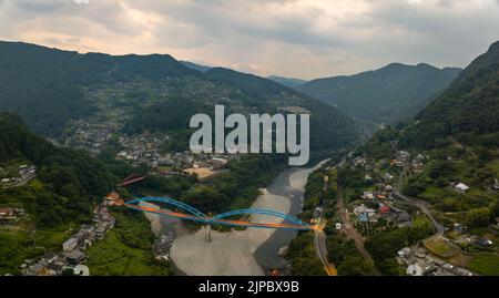 Panorama-Luftaufnahme der blauen Brücke, die ländliche Bergstädte in der Dämmerung verbindet Stockfoto