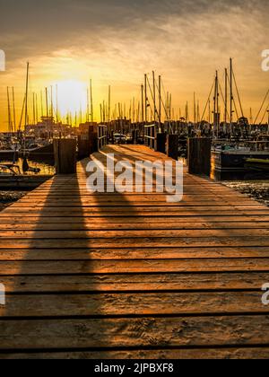 Die Sonne geht über dem Jachthafen von yarmouth auf der Insel wight auf, mit den Spiegelungen der Boote im Wasser Stockfoto