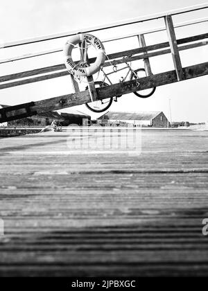 Eine Rettungsboje und ein Fahrrad hängen auf einem Holzsteg über einem Steg am Yachthafen. Stockfoto