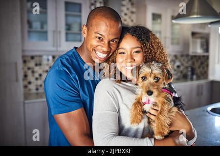 Unsere glückliche Familie. Beschnittenes Porträt eines liebevollen jungen Paares, das mit seinem Welpen zu Hause in der Küche steht. Stockfoto
