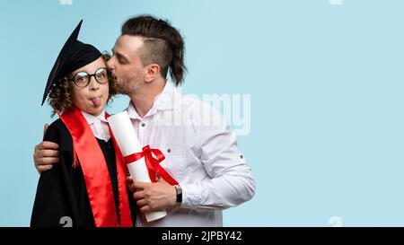 Freudige weibliche Kind in Abschlusskappe und Zeremonie Robe hält Zertifikat zeigt Zunge hat Spaß auf hellblauen Studio Hintergrund. Vater gratuliert Prod Stockfoto