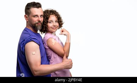 Familie in lässigen T-Shirts mit Bizeps und Pfand nach Impfstoffinjektion im weißen Studio. Vater und Tochter 10-12s gegen Covid-19 geimpft Stockfoto