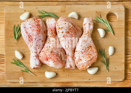 Rohe Hähnchenbeine, mariniert mit Gewürzen, Knoblauch und Rosmarin auf einem Holzschneidebrett. Draufsicht. Stockfoto