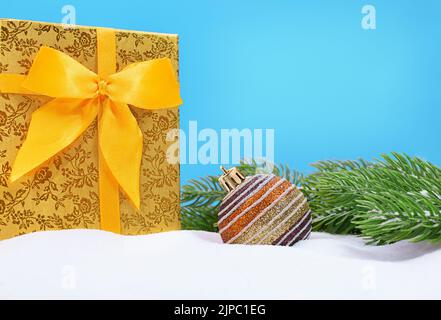 Große gelbe Geschenkbox mit Schleife und glänzenden Ball- und Tannenzweigen auf Schnee. Weihnachten, Neujahr. Speicherplatz kopieren Stockfoto