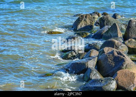 Große Felsbrocken als Wellenbrecher im blauen Meerwasser an der Ostsee nahe dem Ferienort Boltenhagen, Deutschland, Kopierraum, ausgewählter Fokus Stockfoto