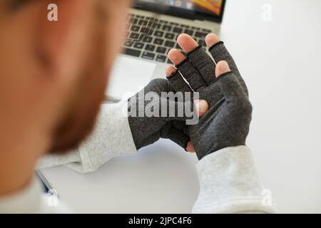 Der junge Mann mit rheumatoider Arthritis trägt Kompressionshandschuhe zur Schmerzlinderung Stockfoto