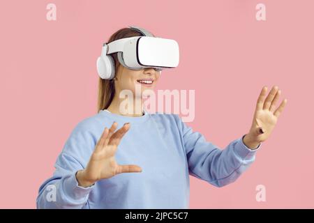 Lächelnd erstaunt junge Frau berühren Luft während VR-Erfahrung, isoliert auf rosa Hintergrund. Stockfoto