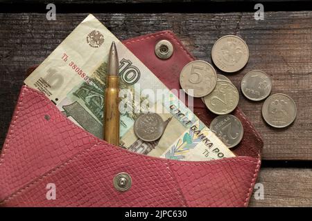 Russische Rubel und eine Kugel liegen in einer Brieftasche auf einem Holztisch, die Finanzierung der Militärarmee, den Krieg stoppen und die Sanktionen 2022 Stockfoto