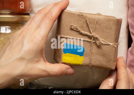 Eine Schachtel mit einer gelb-blauen Flagge der Ukraine in der Hand einer Frau, humanitäre Hilfe für die Ukraine von Menschen Stockfoto