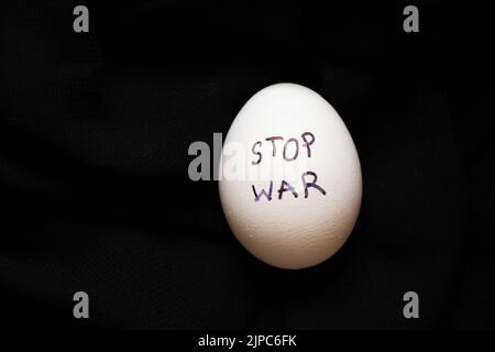 Weißes Hühnerei mit der Aufschrift Stop the war , das auf schwarzem Hintergrund liegt, Essen und Krieg in der Ukraine 2022 Stockfoto