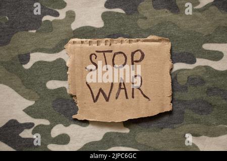 Stop war ist auf Papier geschrieben, das auf der Tarnuniform, Protestaktion, Militärkleidung des Soldaten liegt Stockfoto