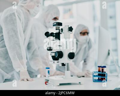 Steriler, weißer und moderner Raum mit einer Nahaufnahme eines Mikroskops und medizinischer Wissenschaftler oder einer Gruppe, die nach Korona forscht. Klinisch und hell Stockfoto