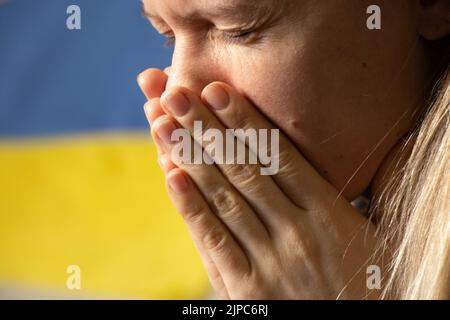 Ukrainische Frau weint vor Trauer und Angst vor dem Hintergrund der Flagge der Ukraine, Angst und Verzweiflung der Menschen in der Ukraine Stockfoto