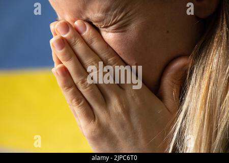 Ukrainische Frau weint vor Trauer und Angst vor dem Hintergrund der Flagge der Ukraine, Angst und Verzweiflung der Menschen in der Ukraine Stockfoto