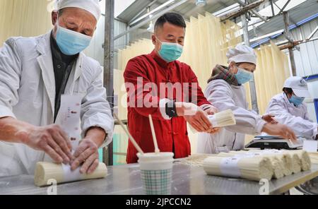 (220817) -- LUONAN, 17. August 2022 (Xinhua) -- Li Changman (1. L) verpackt Nudeln im Dorf Meidi der Gemeinde Bao'an im Landkreis Luonan der Stadt Shangluo, nordwestlich der chinesischen Provinz Shaanxi, 18. März 2022. Li Changman, ein 66-jähriger Dorfbewohner des Dorfes Meidi, hat seit seiner Jugend die einzigartigen Fähigkeiten zur Herstellung von Hohlnudeln erlernt. Er ist der Erbe von Luonan handgefertigten heiligen Nudelherstellung Fähigkeiten, die als ein provinzielles immaterielles Kulturerbe aufgeführt ist. Er ermutigte sein Kind, diese Kunst zu erlernen, und lehrte die Dorfbewohner auch, ihr Einkommen zu erhöhen. (Xinhua/Tao Ming) Stockfoto