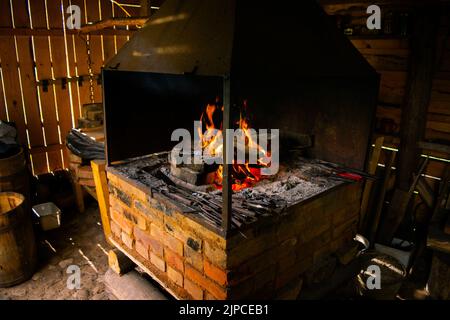 Das Innere einer alten Schmiede. Helles Feuer, das im Ofen brennt. Schmiedet Feuer, das für die Herstellung von Eisenwerkzeugen in Schmieden verwendet wird. Stockfoto