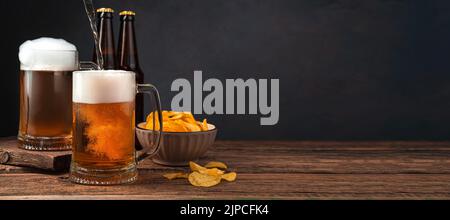 Kaltes Bier in zwei Gläsern und eine Schüssel Kartoffelchips auf dunklem Grund. Stockfoto