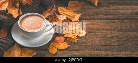 Cappuccino und Herbstlaub auf Holzgrund. Gemütliche Herbstkomposition. Stockfoto