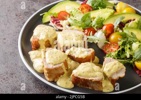 Zartes Schweinefilet mit Honig-Senfsauce und Salat, Avocado- und Tomatensalat in Nahaufnahme auf einem Teller auf dem Tisch serviert. Horizontal Stockfoto