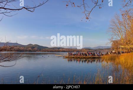 Menschen, die die Wintersonne über dem Pier-Restaurant am See von Banyoles, Girona, Katalonien, Spanien genießen Stockfoto