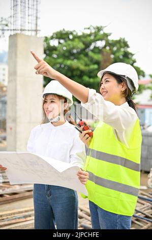 Schöne und professionelle junge asiatische Ingenieurin und Architektin diskutieren und planen den Bauplan auf der Baustelle tog Stockfoto