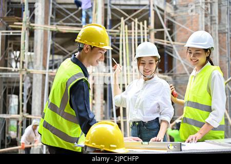 Eine schöne asiatische Geschäftsfrau, die im Freien mit zwei professionellen asiatischen Ingenieuren auf der Baustelle zusammentreffen wird. Stockfoto