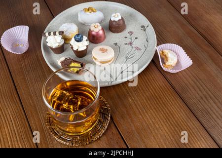 Macaron neben kleinem Schokoladenglas mit Pistazien-Creme, Trüffeln, Walnusskameo und Whiskey-Glas. Stockfoto