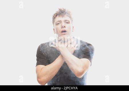 Ersticken Sie im Rauch. Verängstigte junge Mann mit gestressten Emotionen isoliert über weißem Hintergrund mit Wolken aus Rauch. Konzept des Gesichtsausdrucks Stockfoto