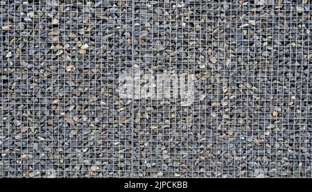 Gabion mit Haufen kleiner Steine in einem Gitter als Stadt- oder Gartendekoration, strukturierter Hintergrund Stockfoto