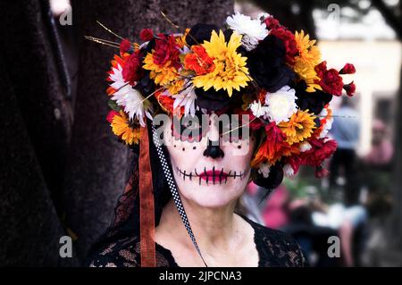 Ein wunderschönes Porträt einer Frau, die am Tag des Todes ein farbenfrohes Totenschädel-Make-up und eine Blumenkrone trägt Stockfoto