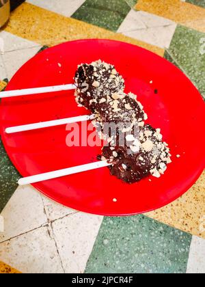 Die Nahaufnahme von drei Schokoladenkuchen knallt auf einem roten Teller, gewürzt mit Krümel Stockfoto