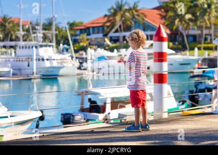 Kinderbeobachtungsyacht und Boot im Hafen. Yachtsport für Familien mit Kindern. Kleiner Junge, der in den Sommerferien in einem tropischen Resort herumläuft. Stockfoto